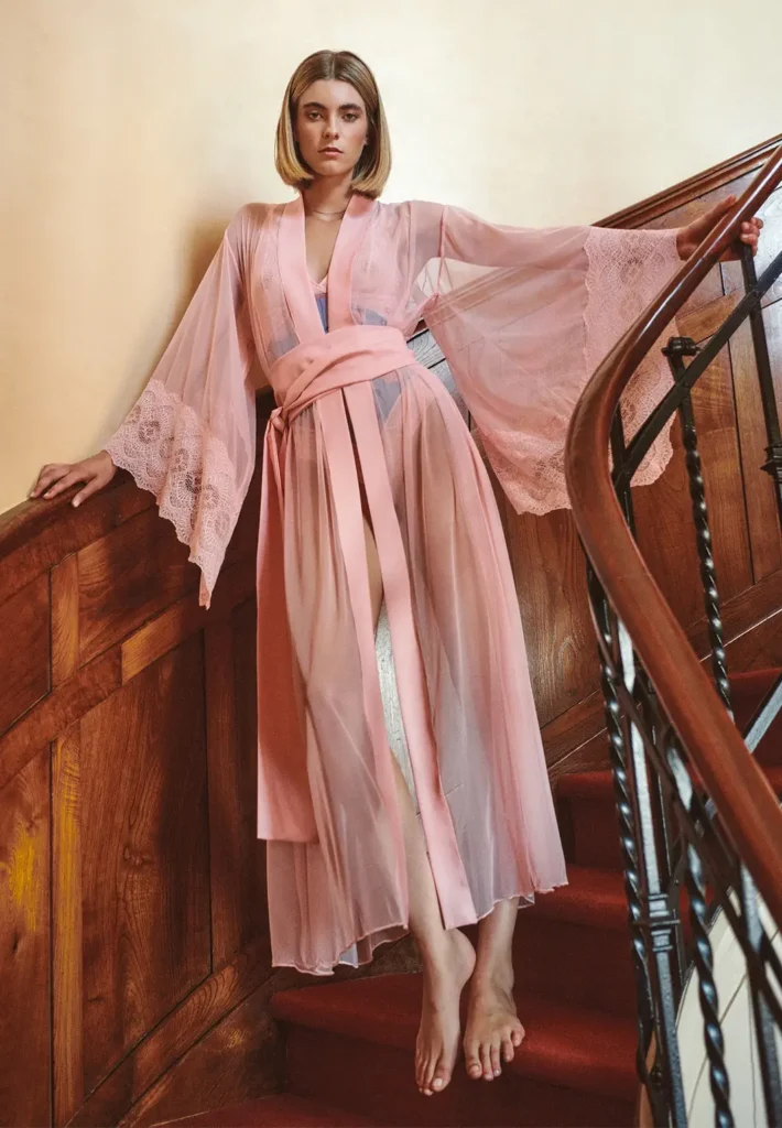 A woman wearing a pink kimono with lace-edged sleeves standing on a spiralling wooden staircase