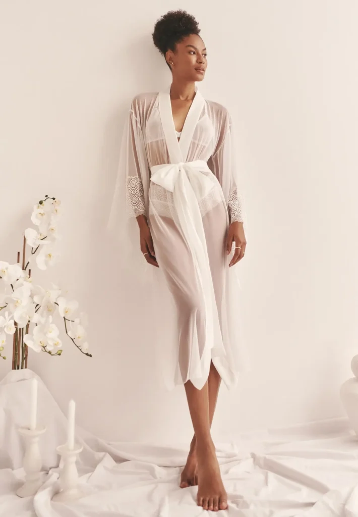 A woman wearing a white kimono with the sash tied in a bow around her waist, leaning back against a wall